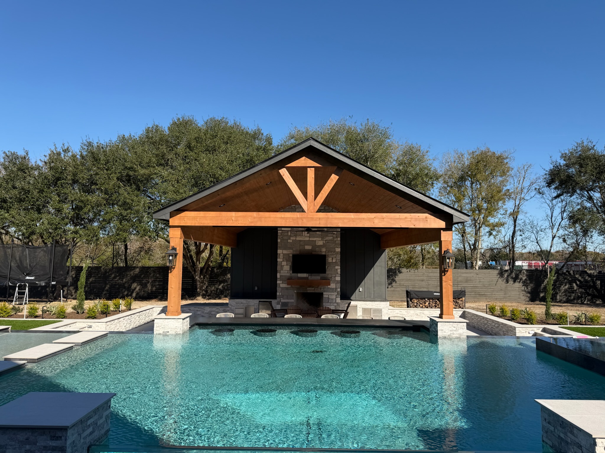 Wooden poolside cabana with stone fireplace on sunny day