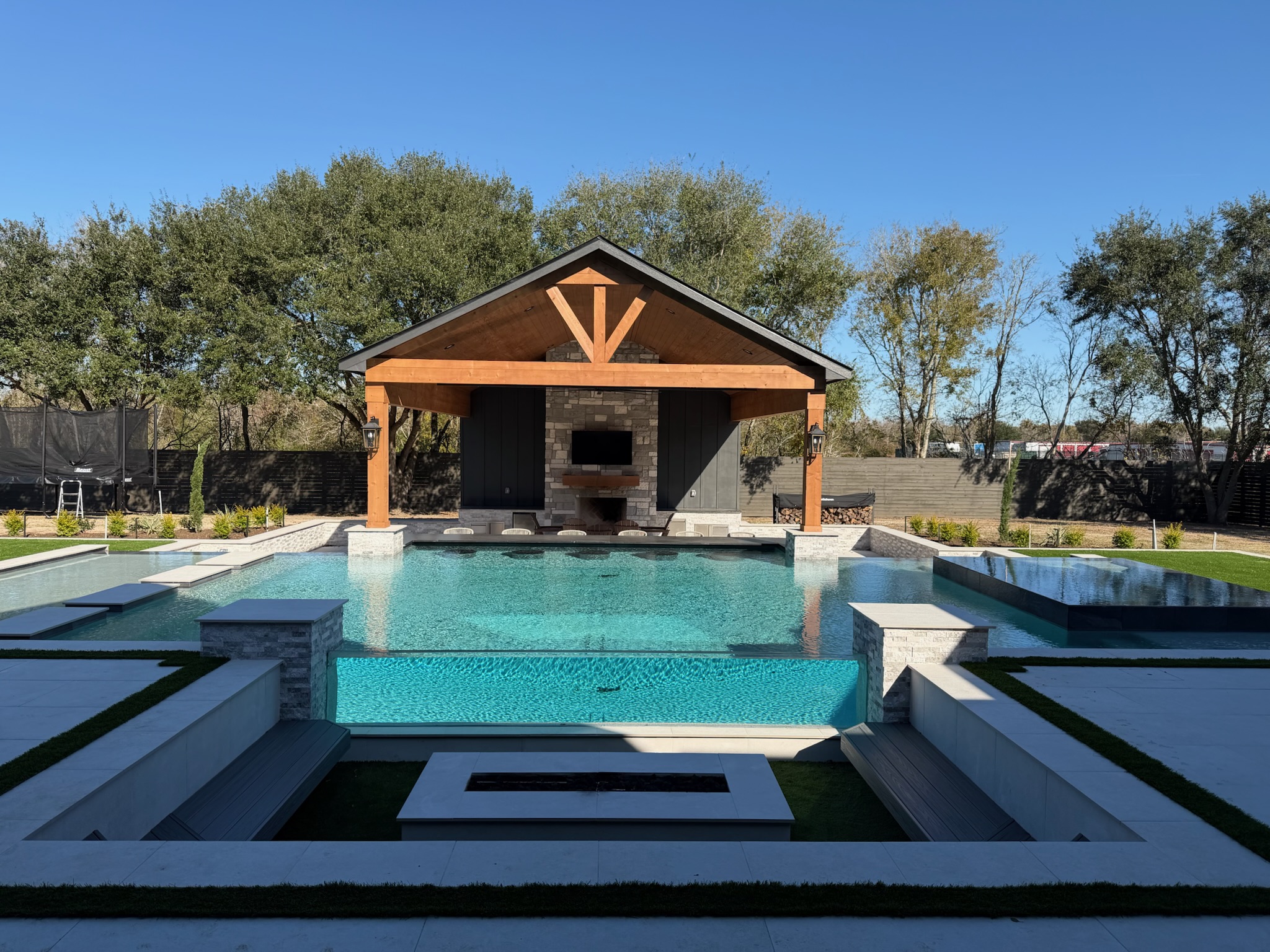 Modern pool with glass wall and wooden pavilion on clear blue day