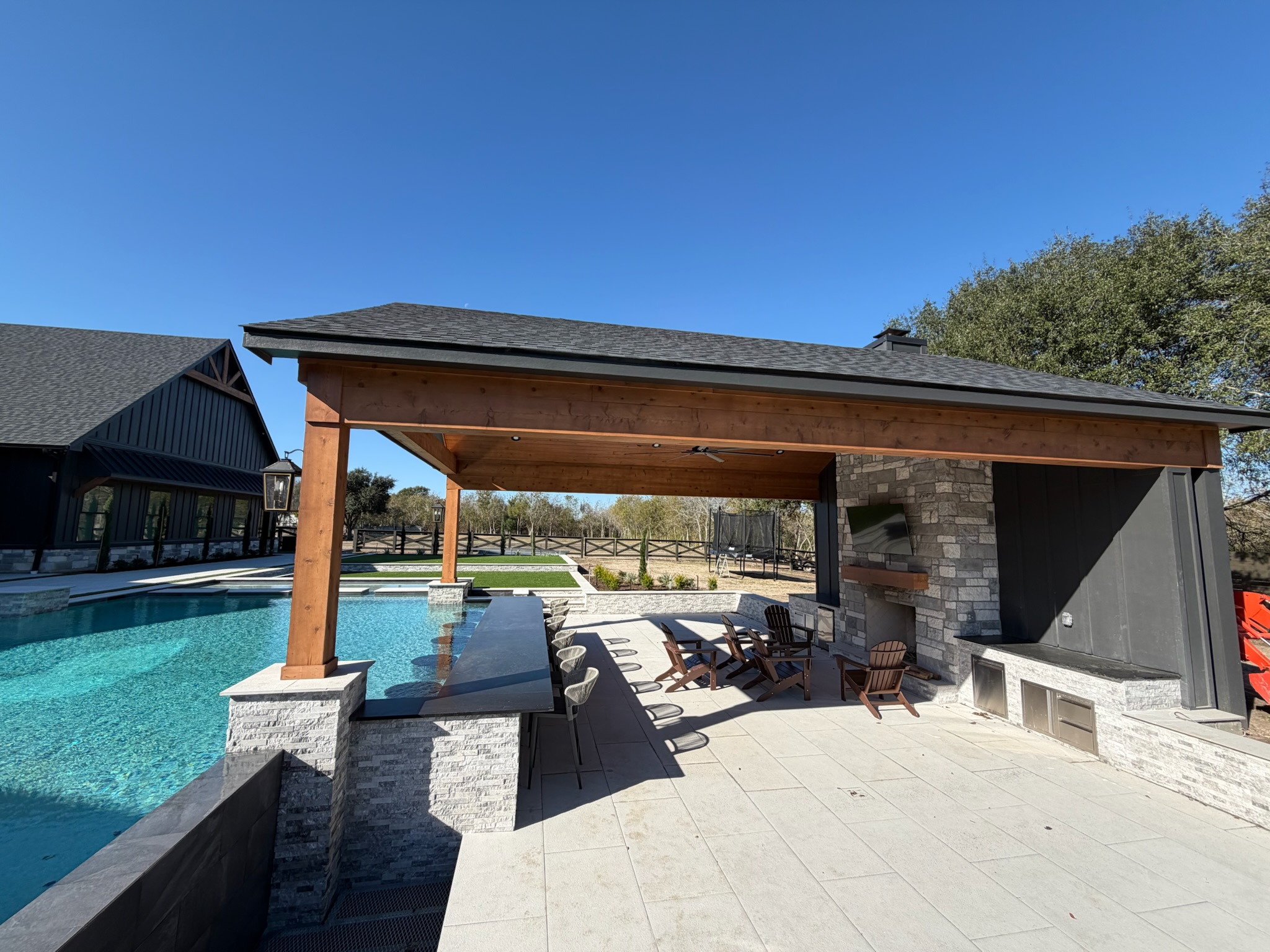 Luxurious backyard with pool, covered patio, and outdoor kitchen on sunny day