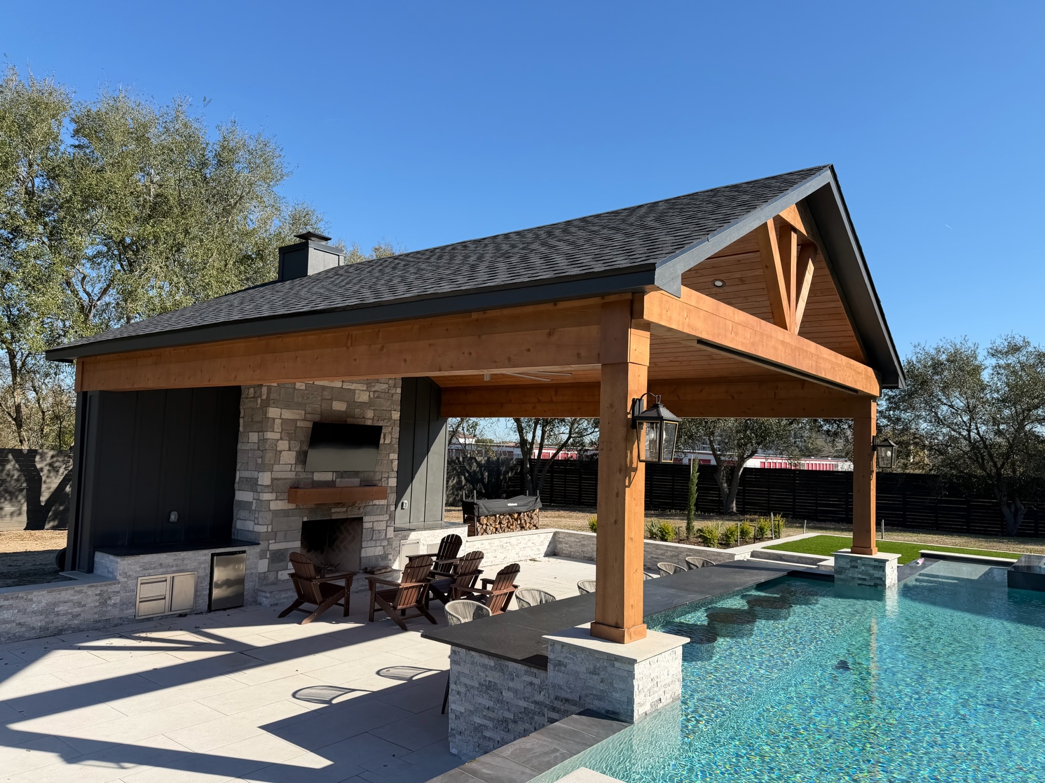 Luxurious poolside pavilion with outdoor fireplace and Adirondack chairs