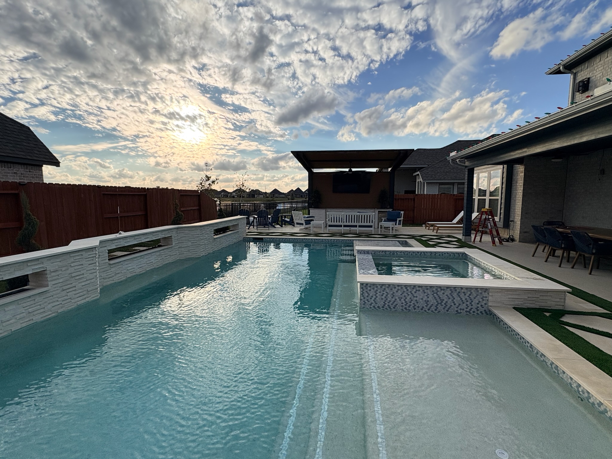 Backyard swimming pool with spa and covered patio at sunset