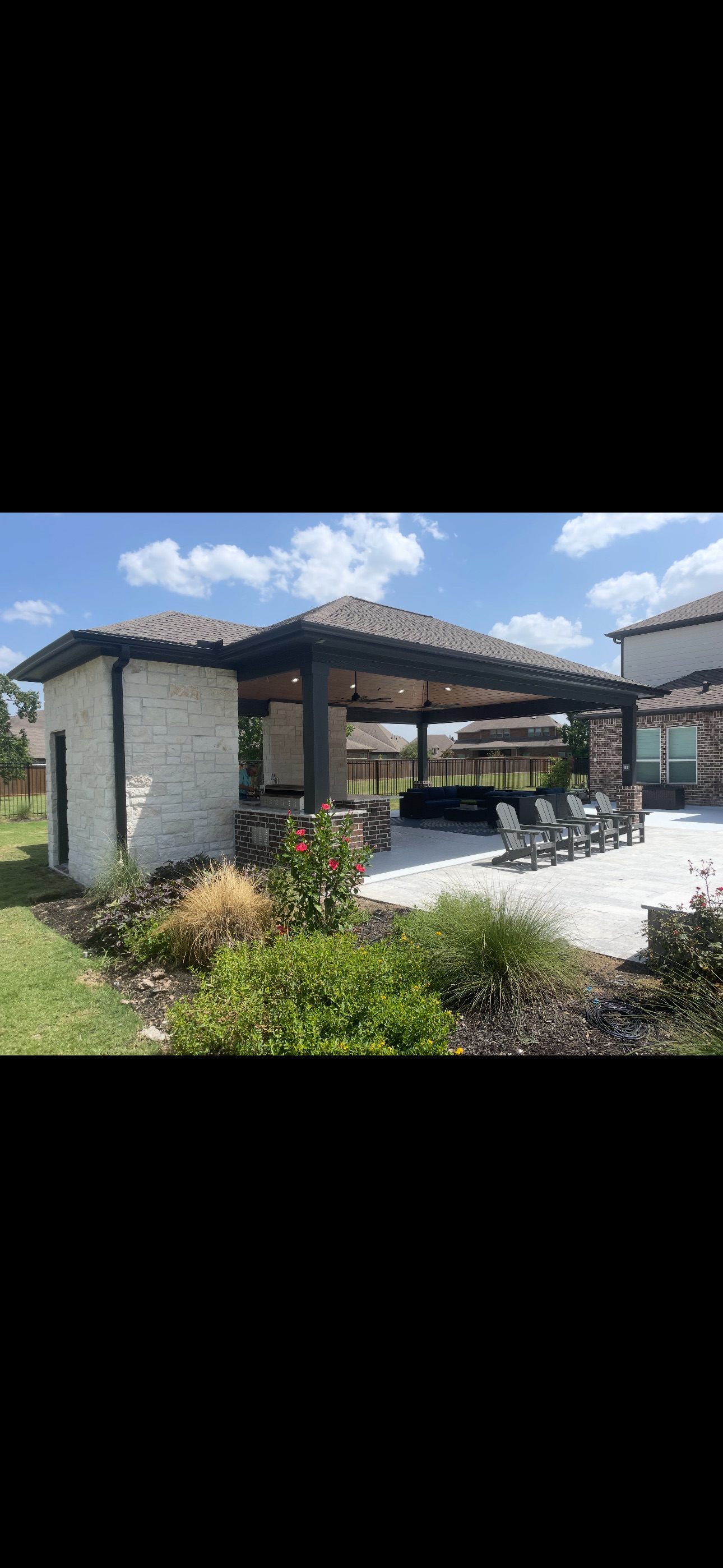 Outdoor patio with covered seating area, landscaped yard, and Adirondack chairs