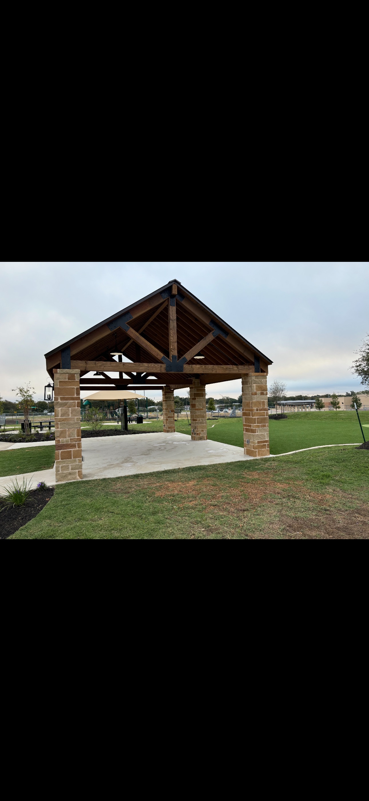 Wooden and stone pavilion with peaked roof in a park-like setting