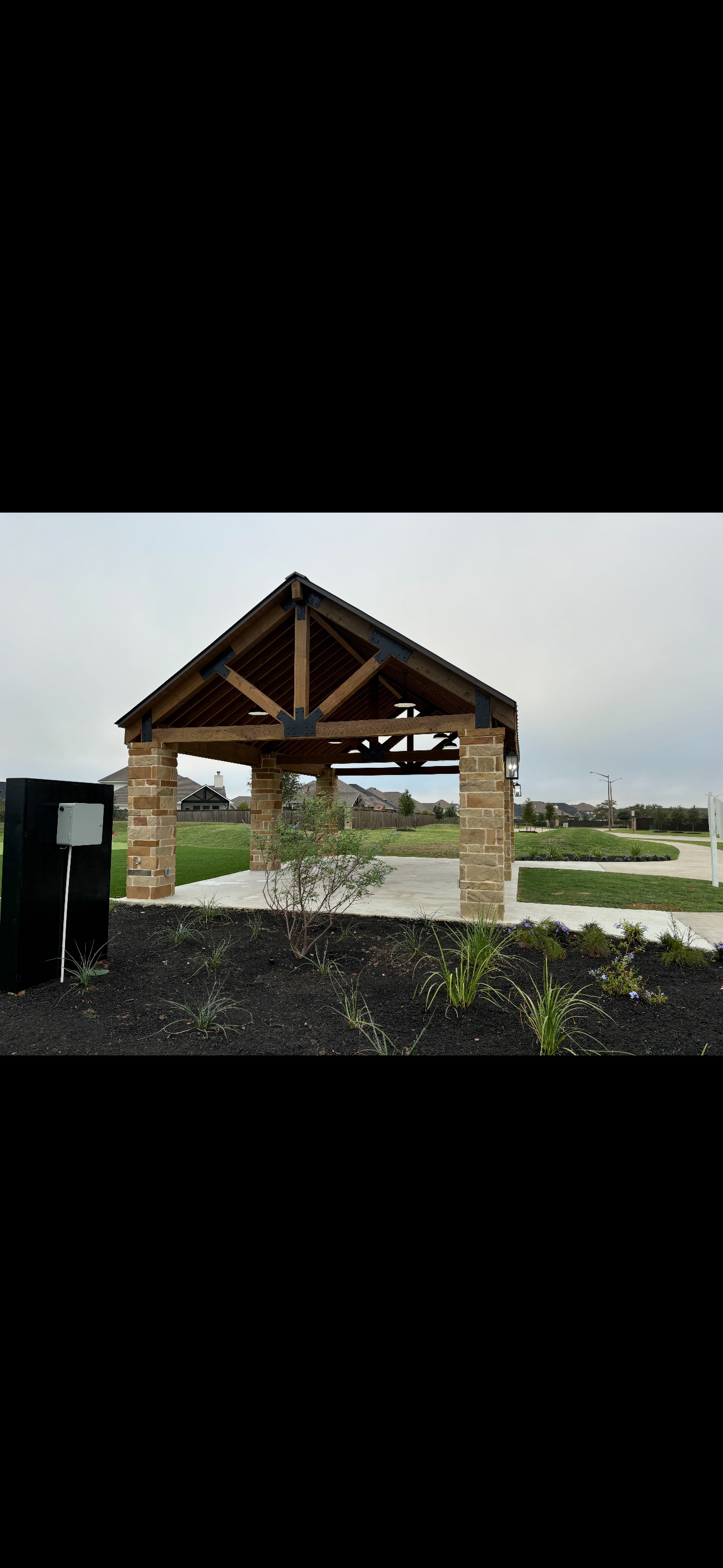 Wooden and stone pavilion with peaked roof in suburban neighborhood park
