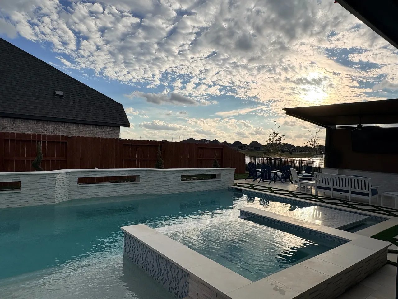 Backyard swimming pool with spa at sunset under dramatic cloudy sky