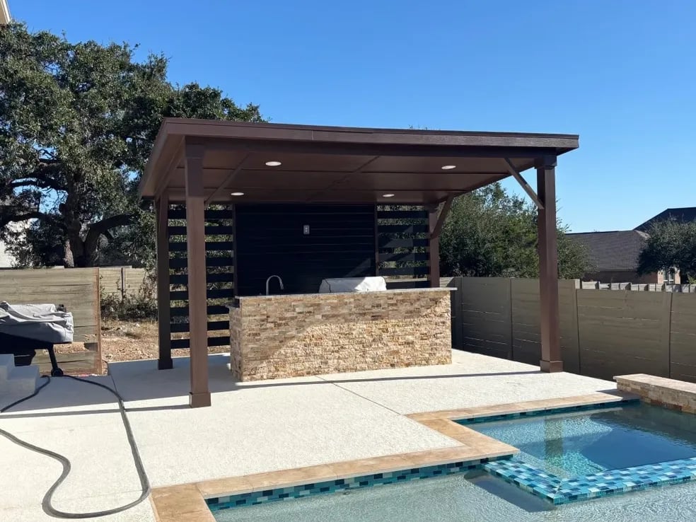 Modern outdoor kitchen with pergola, pool, and stone-clad cooking area