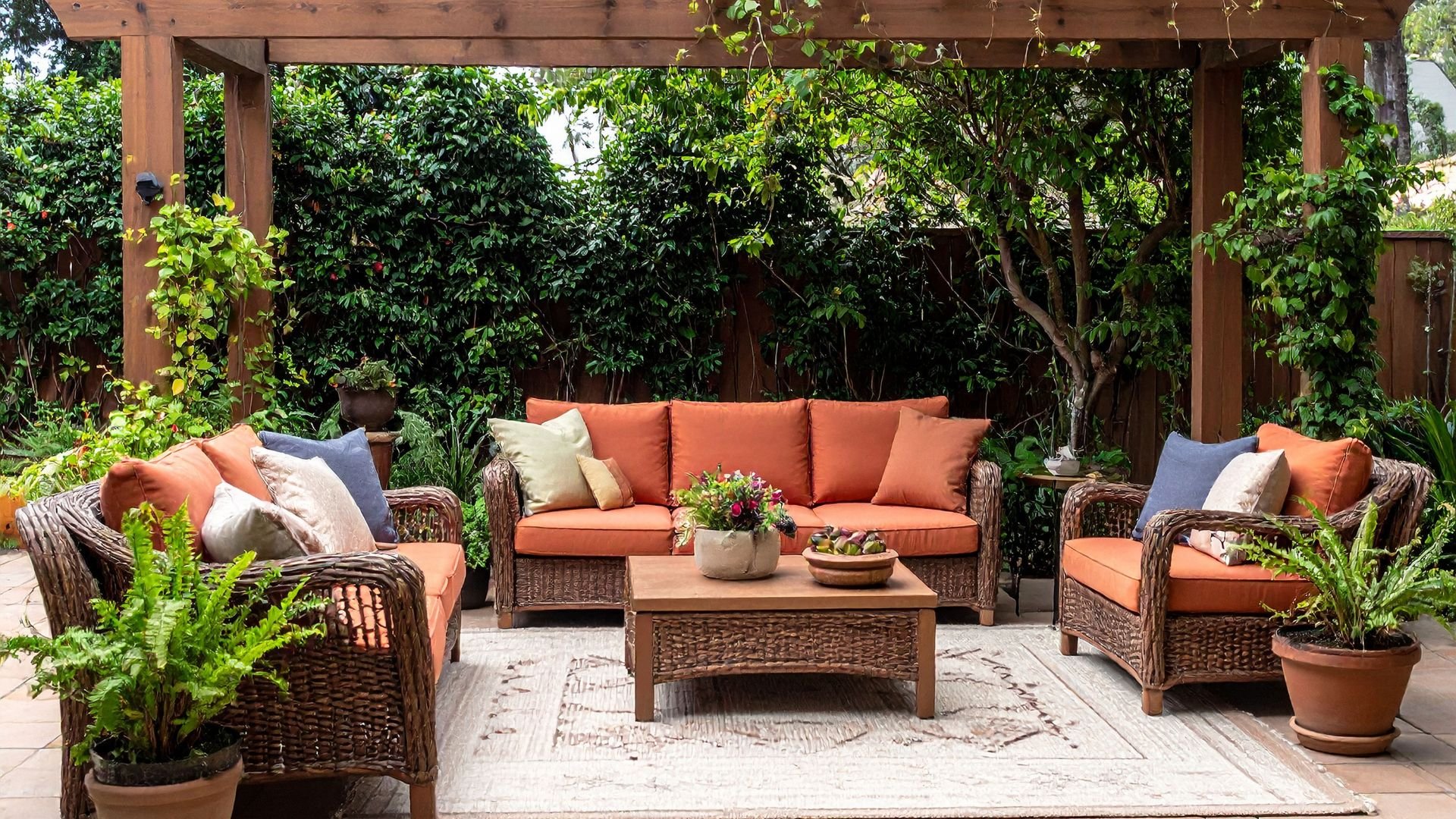 Cozy outdoor patio with wicker furniture, orange cushions, and lush green plants