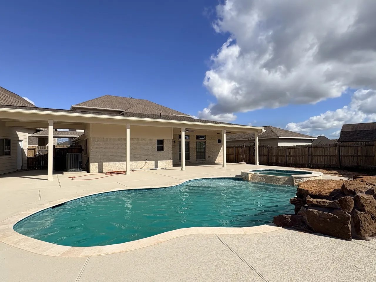 Backyard with turquoise swimming pool, spa, and covered patio on sunny day